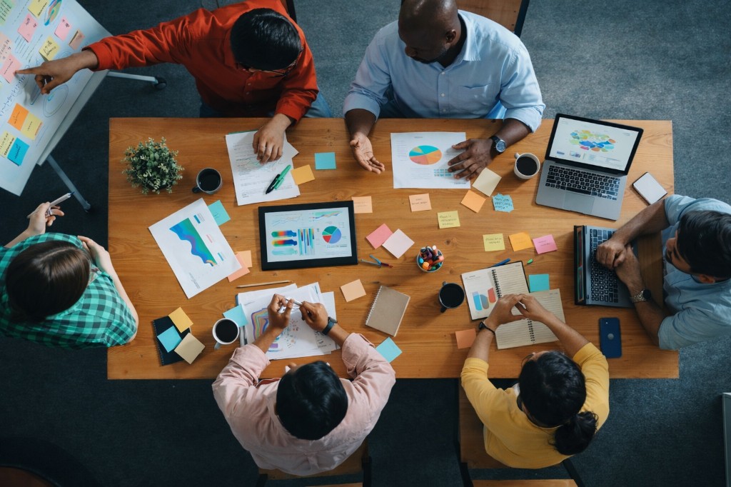 Bird’s-eye view of a diverse team collaborating around a table with charts, laptops, and workshop materials